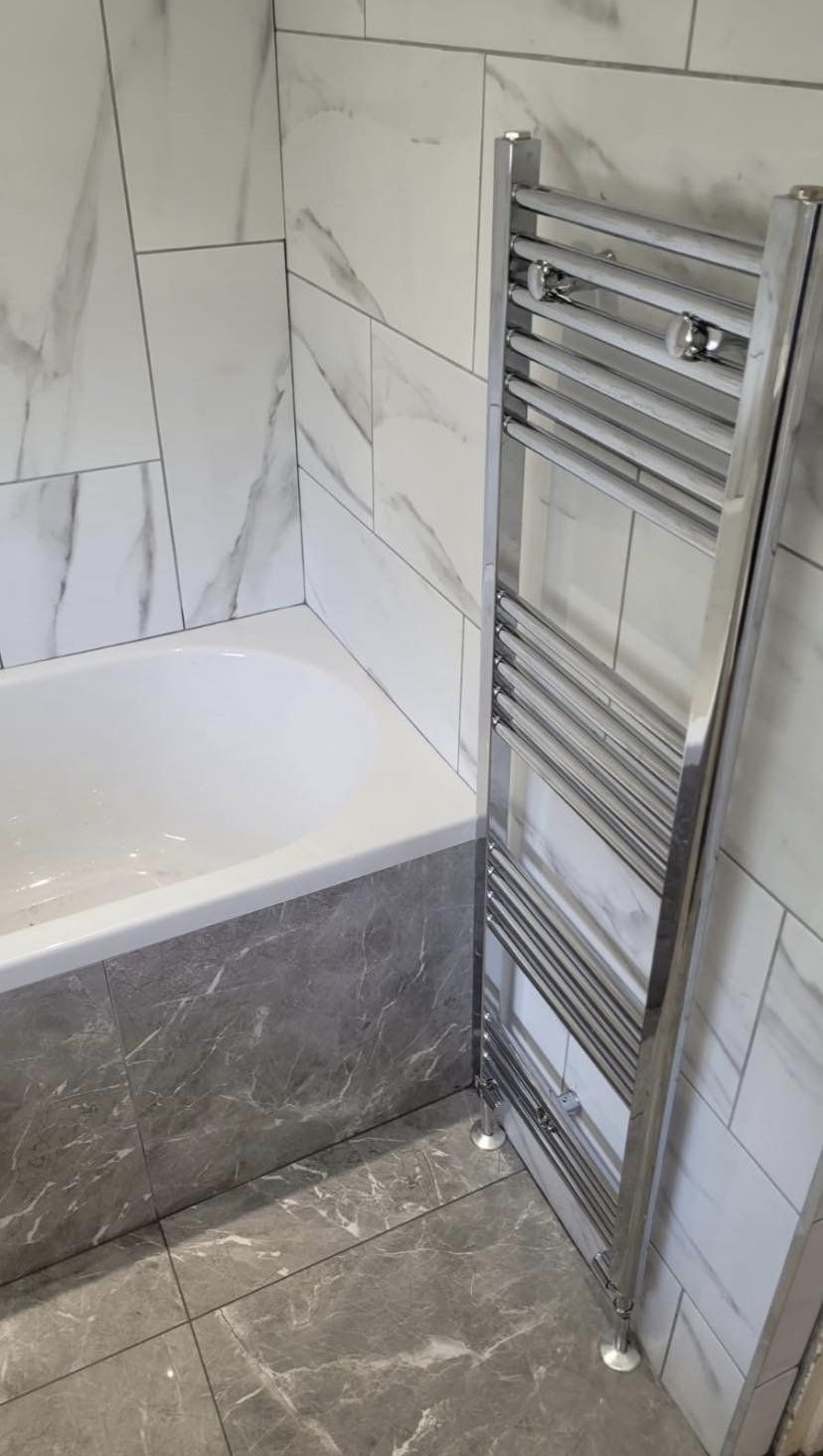 A chrome towel rail beside a new bath, with marble-effect wall tiles