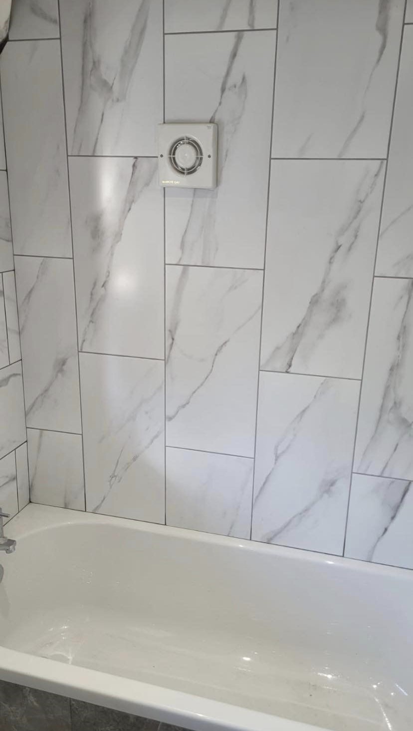 Marble-effect tiles above a new bath, with an extractor fan