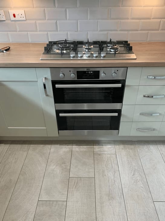 A gas hob above a double oven in a kitchen with metro tiles