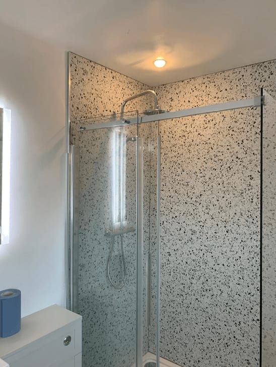 A shower enclosure lined with terrazzo-effect panels