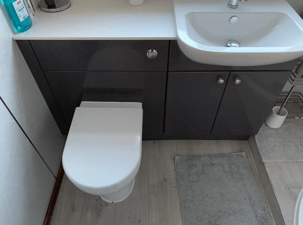 A dark fitted vanity unit with a basin and WC on a pale floor